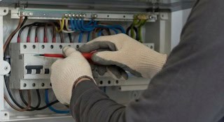 Elektriker schließt Leitungen in einem geöffneten Sicherungskasten an
